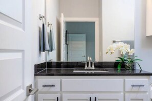 Un baño con encimera negra, muebles blancos, un espejo y una orquídea en maceta.
