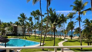 A pool surrounded by palm trees and a beach view. - Playa Palmera Beach Front Apartments (Punta Cana)