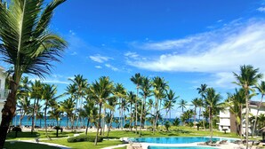 A resort with a swimming pool, palm trees, and a view of the ocean. - Playa Palmera Beach Front Apartments (Punta Cana)