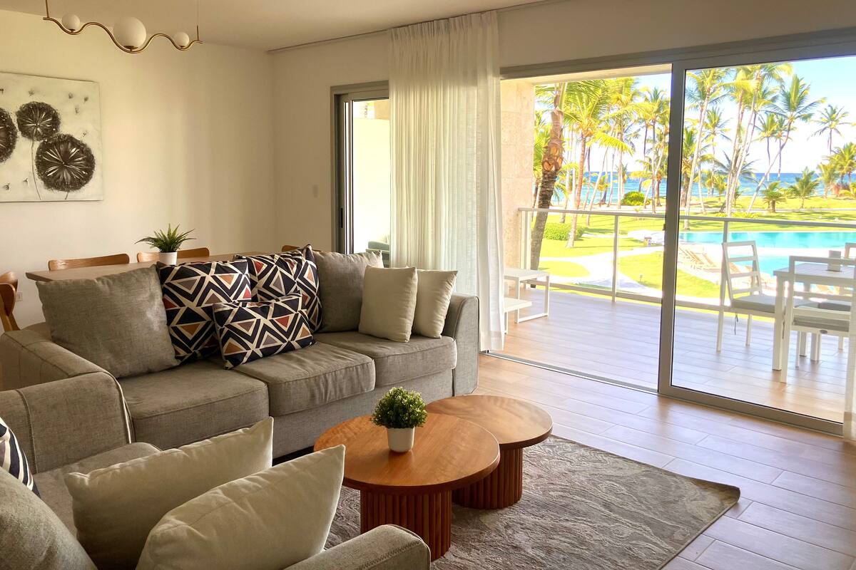 Ein modernes Wohnzimmer mit Sofa, Couchtisch und Blick auf Pool und tropische Landschaft.
