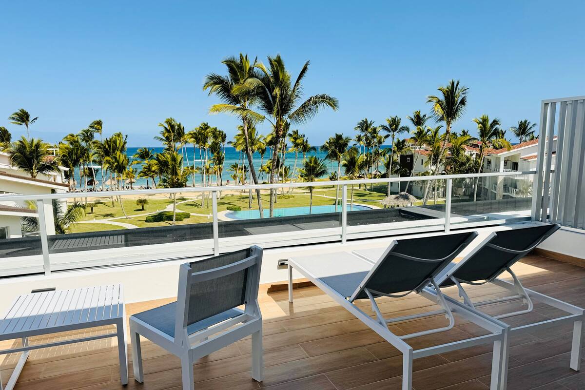Ein Balkon mit zwei Liegestühlen, einem Pool und Blick auf Strand und Meer.