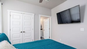 A bedroom with a teal bedspread, white doors, and a mounted TV. - H3/H5 Spacious & Urban Modern Condo - 2 units! (Oklahoma City)