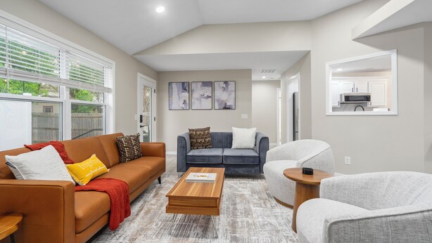 A modern living room with a brown sofa, a blue sofa, and a grey armchair. There is a wooden coffee table in the center.