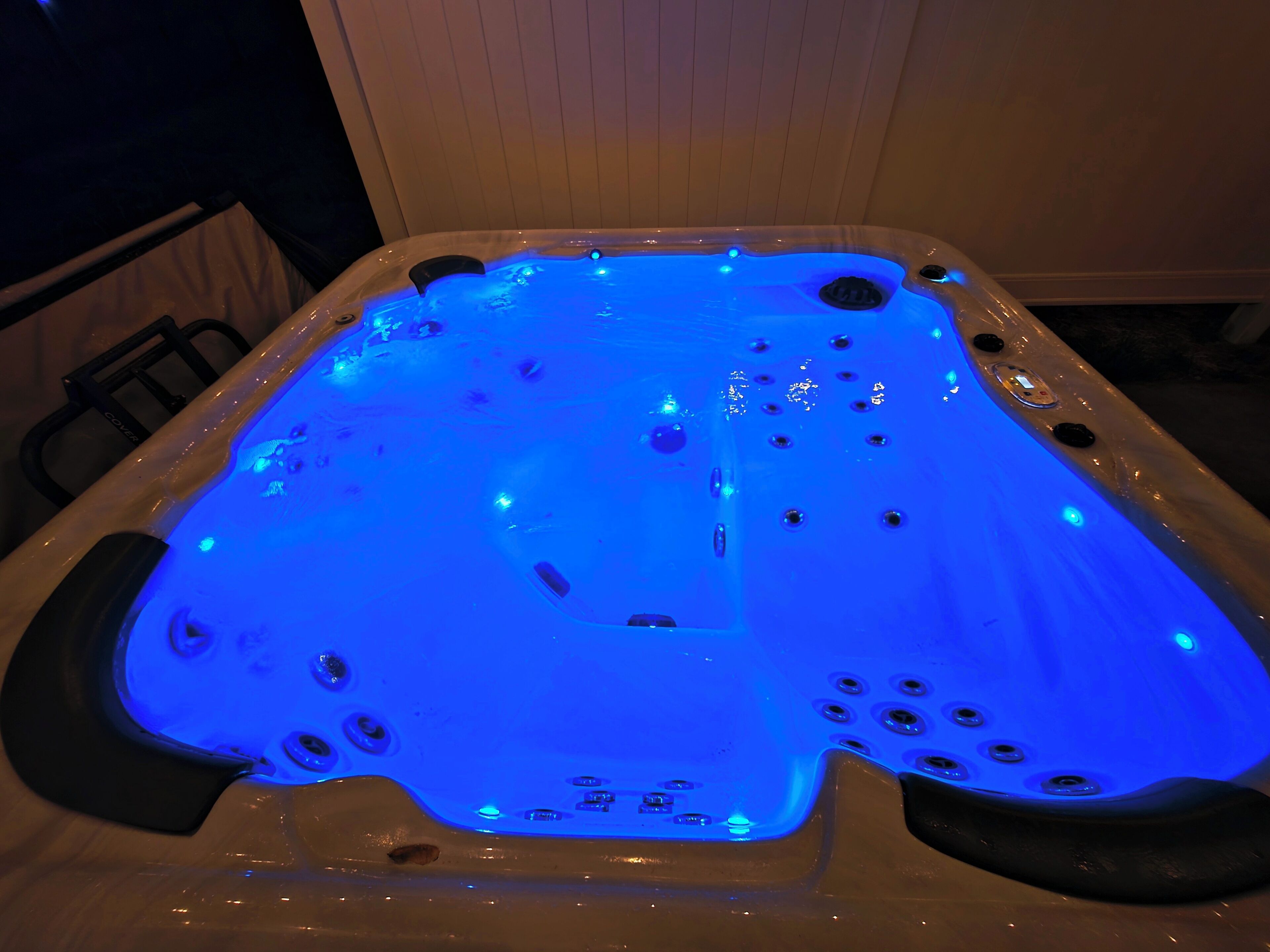 Ein Whirlpool mit blauer LED-Beleuchtung, mehreren Düsen und einem Bedienfeld.