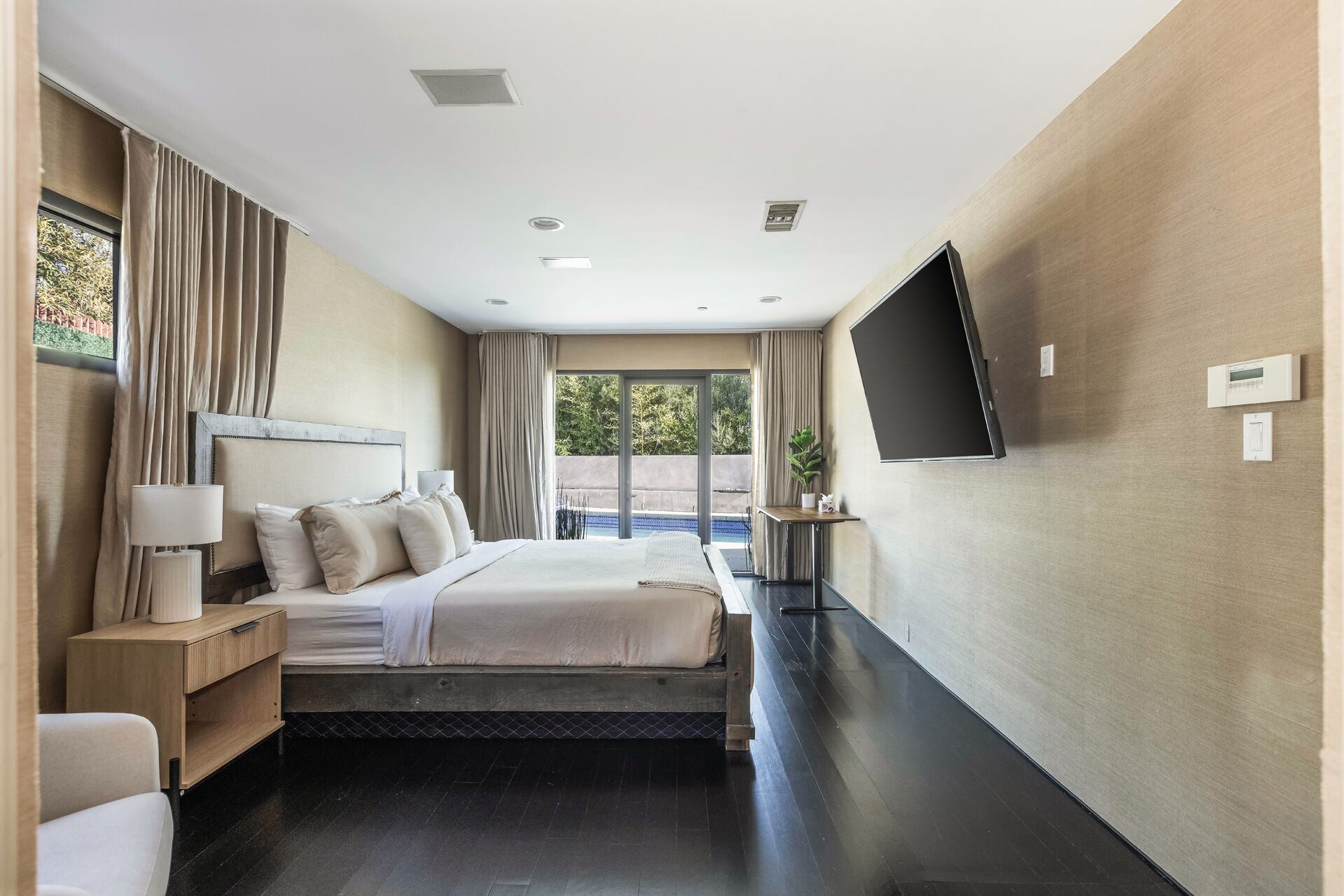 Una habitación de hotel moderna con una cama grande, un televisor en la pared y vista a una piscina por la ventana.
