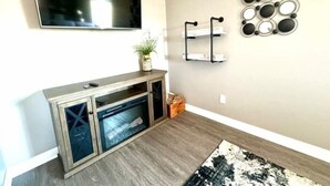 Un salon avec un téléviseur à écran plat fixé au mur, un meuble en bois doté de portes en verre, une petite plante posée sur le dessus, et un élément décoratif mural.
