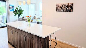 A modern kitchen with a central island, pendant lights, and a cityscape painting on the wall. - New Oceanfront Luxury Suite with a breathtaking  view of downtown Vancouver, (Bowen Island)