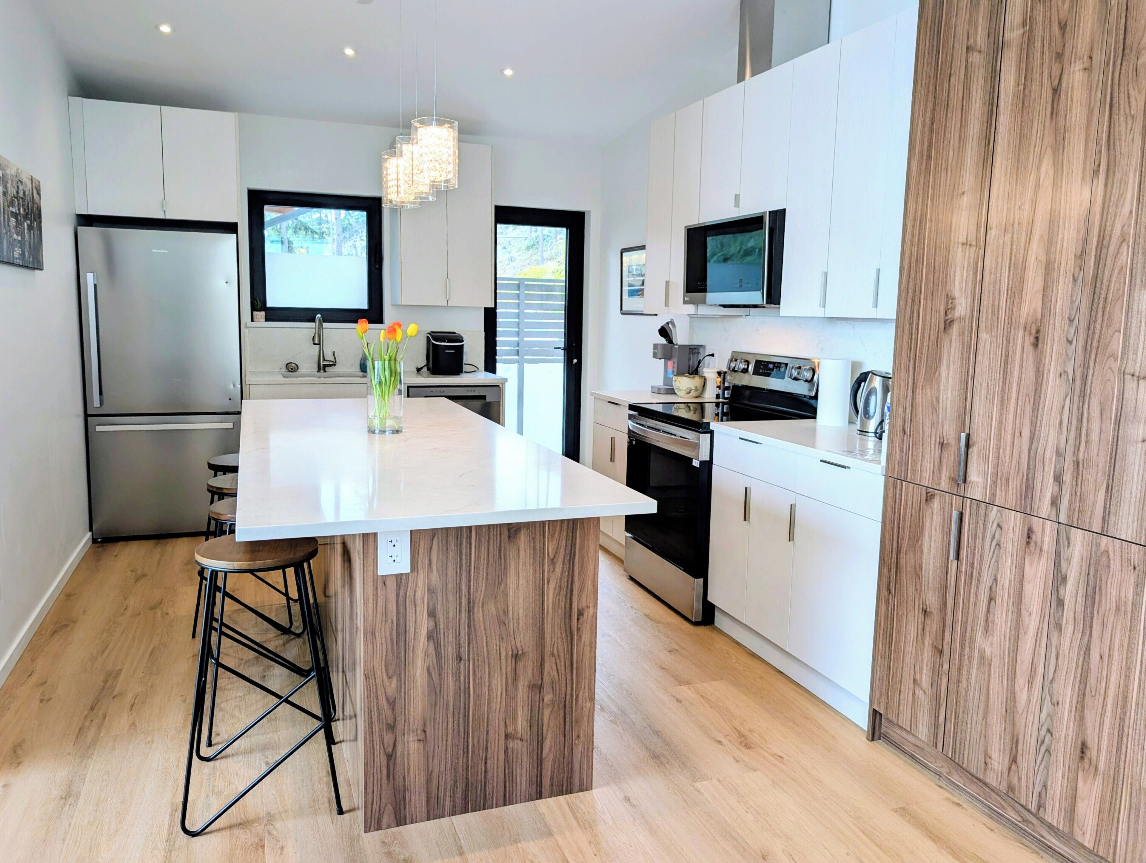 A modern kitchen with white cabinetry, a central island, stainless steel appliances, and a wooden accent wall.
