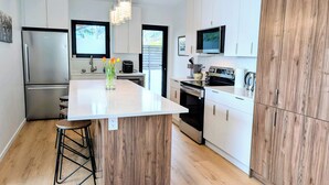 A modern kitchen with white cabinetry, a central island, stainless steel appliances, and a wooden accent wall. - New Oceanfront Luxury Suite with a breathtaking  view of downtown Vancouver, (Bowen Island)