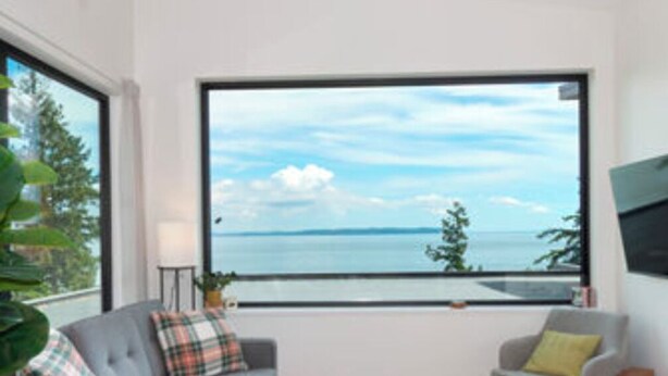 A modern living room with a sofa, armchair, ottoman, and a large window offering a view of the sea. - New Oceanfront Luxury Suite with a breathtaking  view of downtown Vancouver, (Bowen Island)