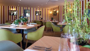 Un restaurante con paredes a rayas, sillas verdes, mesas de madera y plantas en macetas.