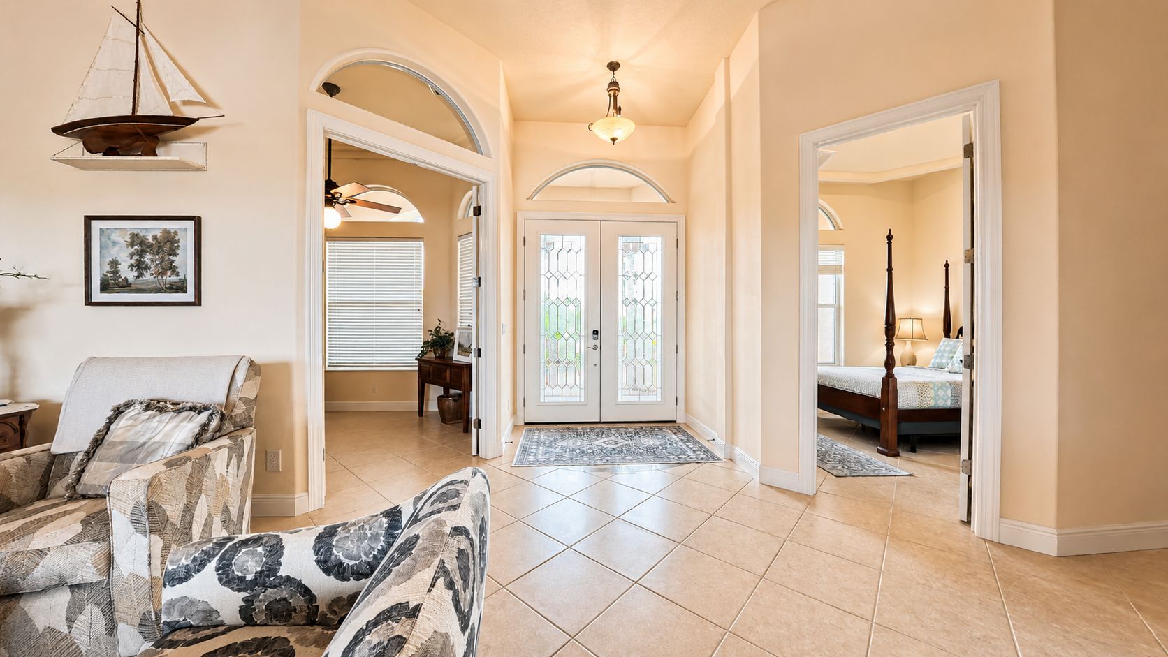A spacious hallway with a large door leading to a bedroom, a dining area with a chair, and a ceiling fan.