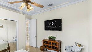Ein Zimmer mit einem Bett, einer Holzkombination, einem Fernseher mit der Aufschrift "VACATION RENTALS CAPE CORAL" und einem Deckenventilator.