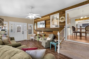 A living room with a wooden wall, a ceiling fan, and a sign for 'iTrip Panama City Beach'. - The Love Shack (Panama City Beach)