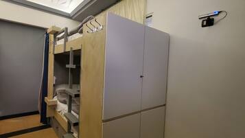 A hotel room with a bunk bed, a wardrobe, and a wall-mounted charging station.