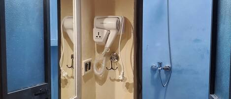 A bathroom with a sink, mirror, hairdryer, and shower.