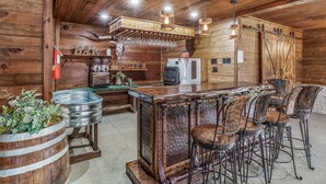 A rustic bar area with wooden walls, a bar counter, stools, and a refrigerator.