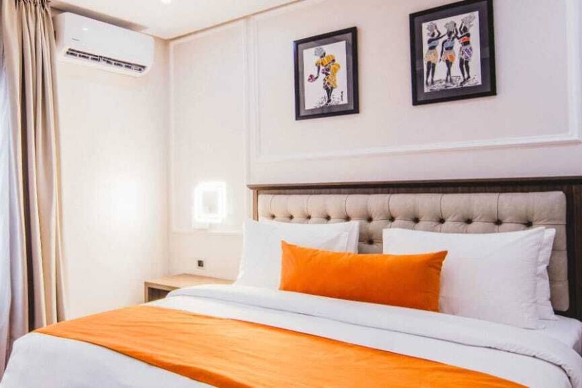 A hotel room with a large bed, beige curtains, and two framed pictures on the wall.