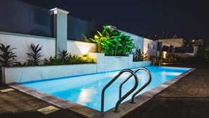 A swimming pool with metal railings, surrounded by plants and a white wall. - MISAN HOTEL (Lekki)