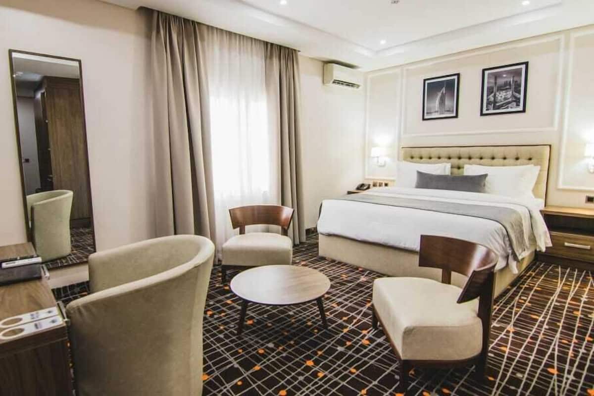 A hotel room with a bed, two armchairs, a small round table, a desk with a telephone, and a mirror.