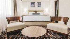 A hotel room with a bed, two armchairs, a round coffee table, and a patterned floor. - MISAN HOTEL (Lekki)