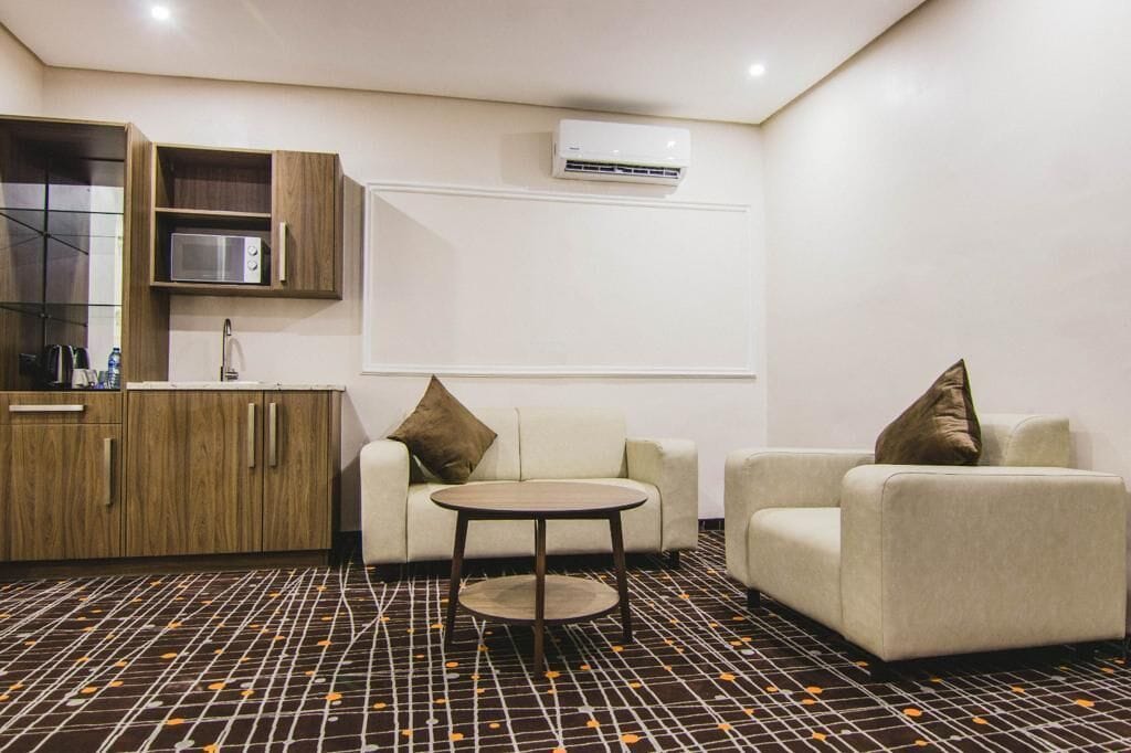 A modern hotel room with a sofa, a small round table, and a kitchenette with a microwave.