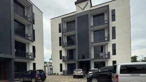 A modern building with multiple balconies and a parking area with several cars. - Casa JV Poolhouse 2-Bed Apartment, Dar es Salaam (Dar es Salaam)