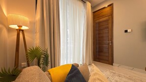 A room with a sofa, a floor lamp, a potted plant, and a wooden door. - Casa JV Poolhouse 2-Bed Apartment, Dar es Salaam (Dar es Salaam)
