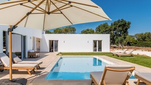 A modern pool area with lounge chairs and a large umbrella.