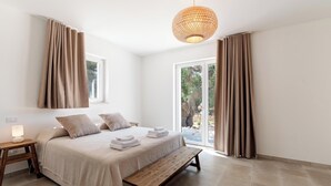 A bedroom with a bed, bench, bedside table, lamp, and curtains.