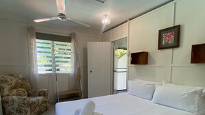 Ein Hotelzimmer mit Bett, Stuhl, Deckenventilator, Tür und einem Fenster mit Vorhängen.