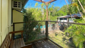 Ein Balkon mit hölzernen Sitzgelegenheit, Metallgeländer und Blick auf einen umzäunten Außenbereich mit Bäumen und einem Gebäude.