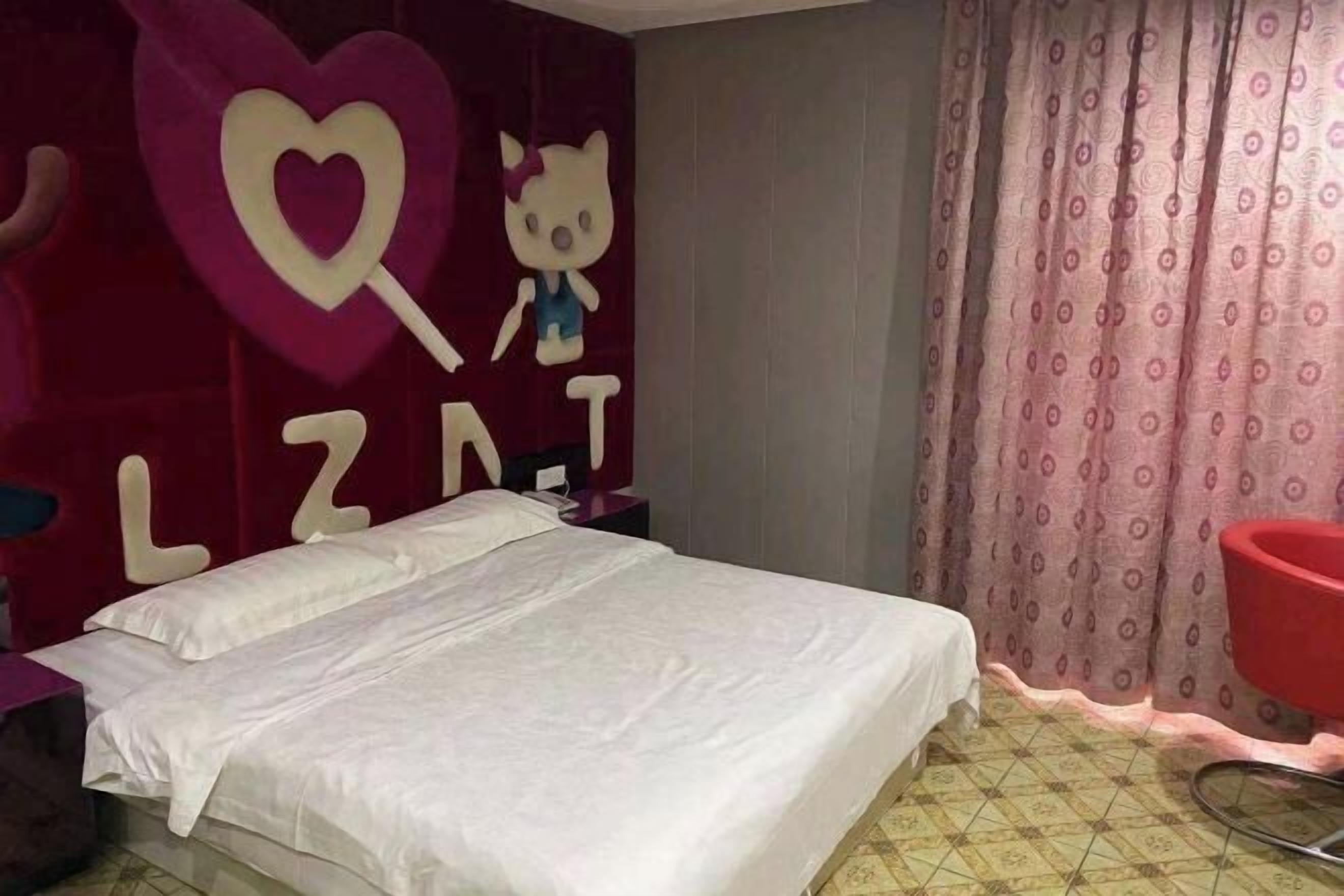 Un dormitorio con una cama, una silla roja, una pared con un corazón y letras, y una cortina estampada.