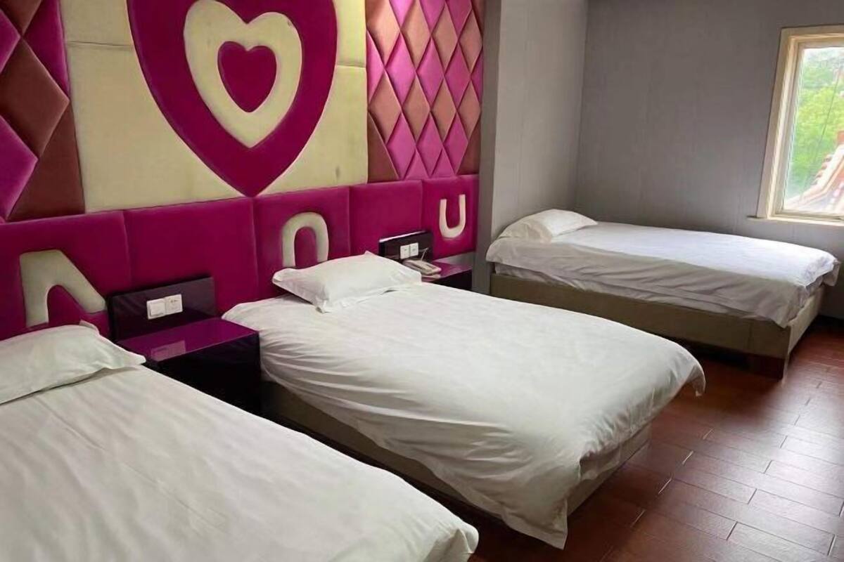 Une chambre d’hôtel avec trois lits, un grand motif en forme de cœur sur la tête de lit et une fenêtre donnant sur un beau paysage.