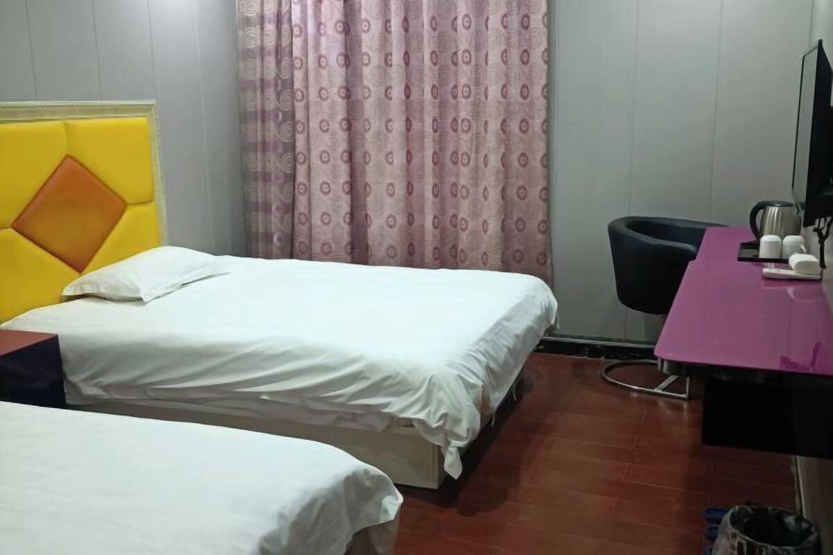 Une chambre d’hôtel avec deux lits, un bureau avec une chaise, une télévision et une fenêtre avec des rideaux.