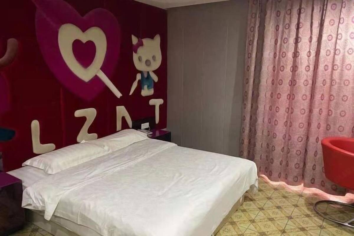 Une chambre à coucher avec un lit, une chaise rouge, une décoration à l’effigie de Hello Kitty et un rideau à motifs.