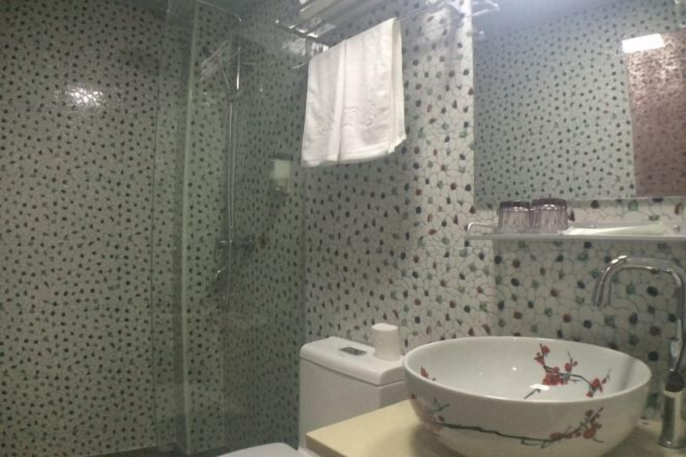 Un baño con cabina de ducha de vidrio, inodoro, lavamanos con lavabo de diseño floral y espejo.
