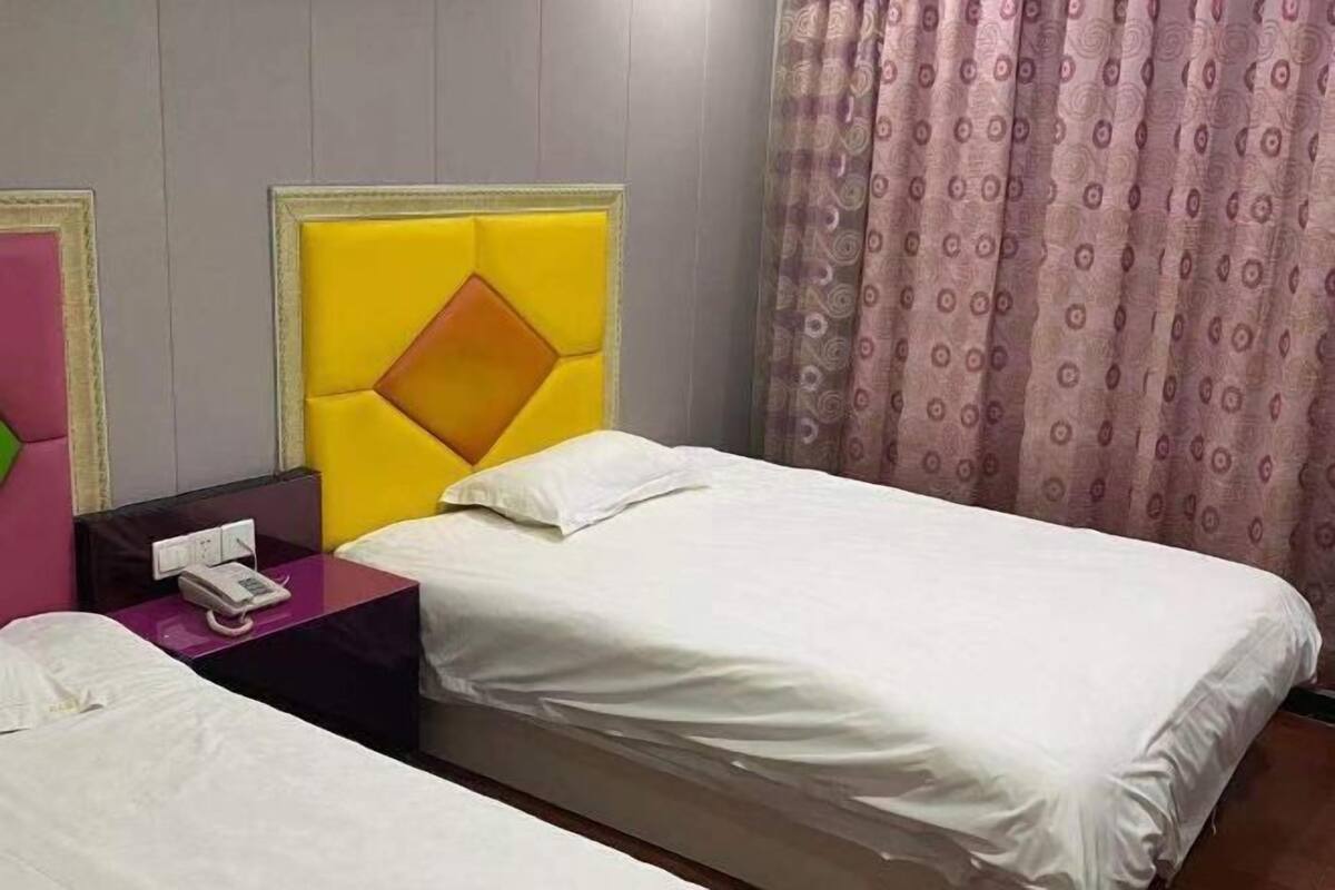Une chambre d’hôtel avec deux lits, un téléphone sur une table de chevet violette et un rideau à motifs.