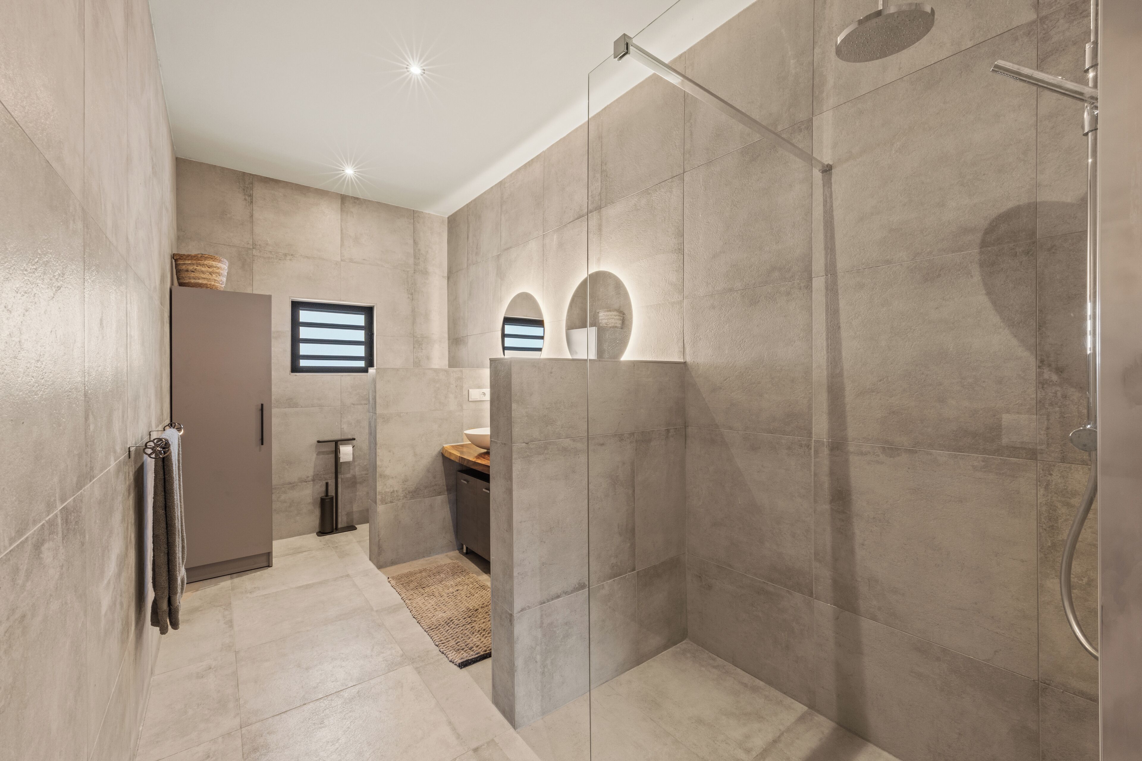 Un baño moderno con ducha envuelta en vidrio, lavamanos empotrado y toallero.