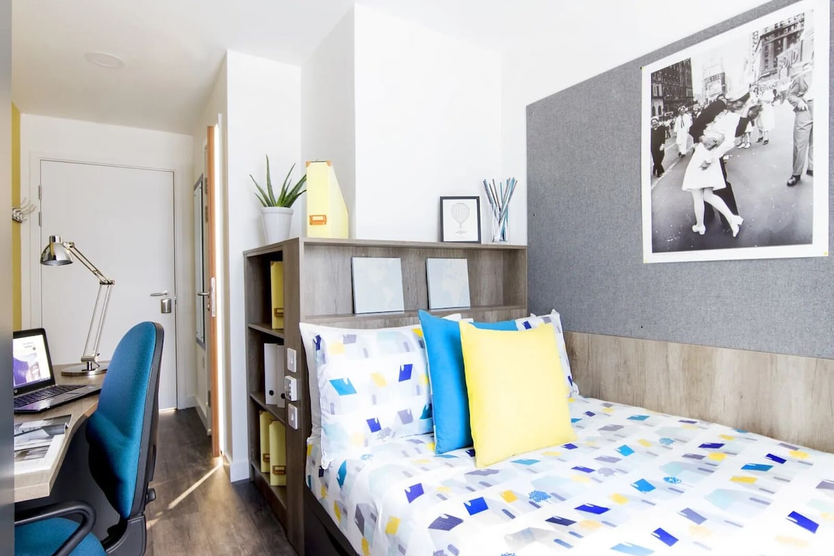 A modern hotel room with a bed, a desk, and a bookshelf.