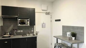 A compact kitchen with dark cabinets, a microwave, a sink, and a small bar area with stools.