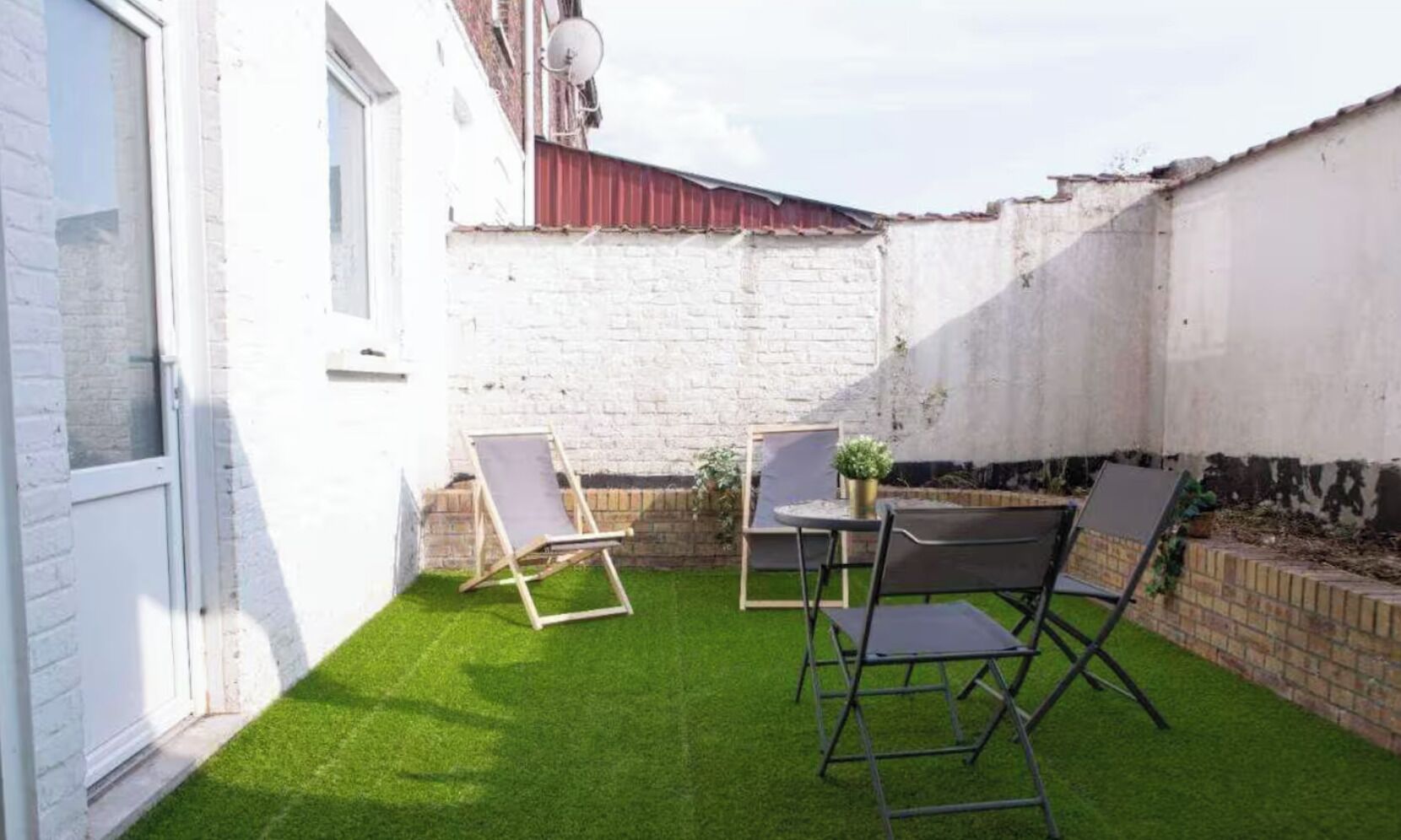 A small backyard with artificial grass, a table, two chairs, and a potted plant.