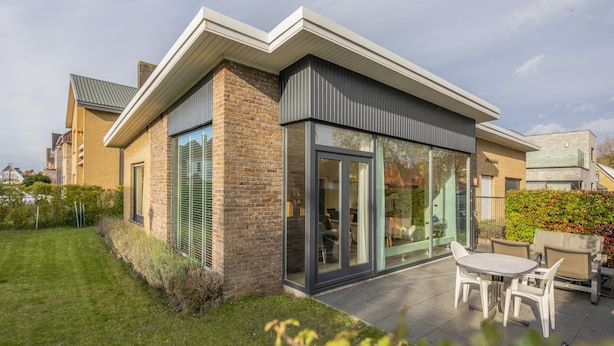 A modern house with a brick exterior, large sliding glass doors, and a patio with outdoor furniture.