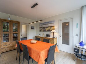Een eethoek met een tafel voor vier personen, een houten kast met glazen deuren, een schilderij aan de muur en een deur met een geëtste glaspanelen.