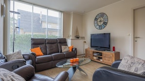 A modern living room with a leather sofa, a glass coffee table, a wooden TV stand, and a large wall clock.