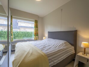 Een slaapkamer met een bed, een nachtkastje met een lamp, een raam met gordijnen en een radiator.