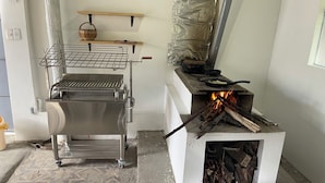 Una cocina con una parrilla de acero inoxidable, una olla sobre una estufa con fuego, y un estante con una cesta.