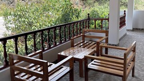 Un espacio de estar al aire libre techado, con bancos y mesas de madera, piso de baldosas y vistas a un paisaje montañoso.