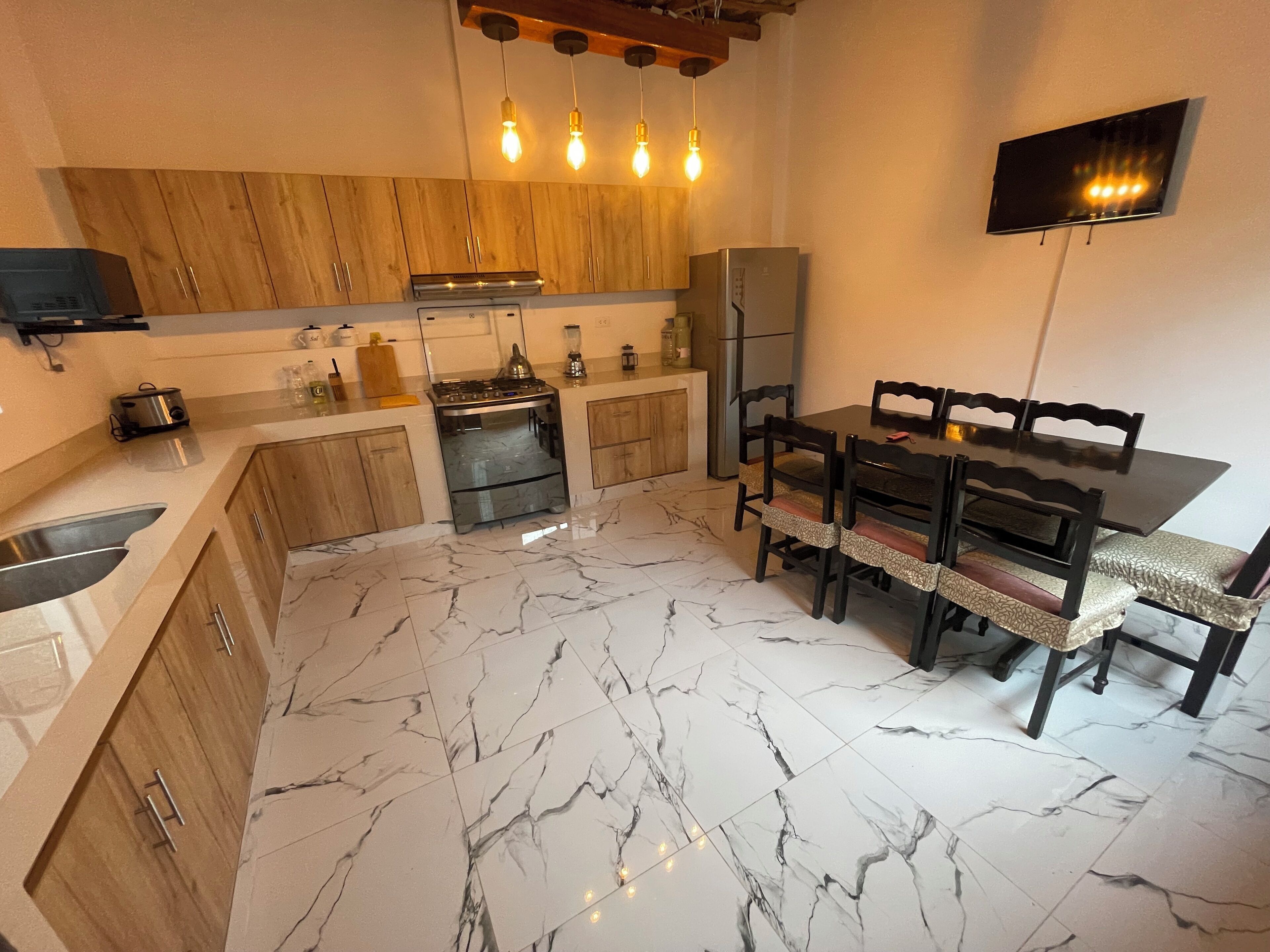 Una cocina compacta con armarios de madera, horno integrado, una mesa de comedor con sillas y un televisor de pantalla plana montado en la pared.