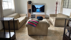 Una sala de estar con dos sofás, un televisor, un altavoz y un perchero.